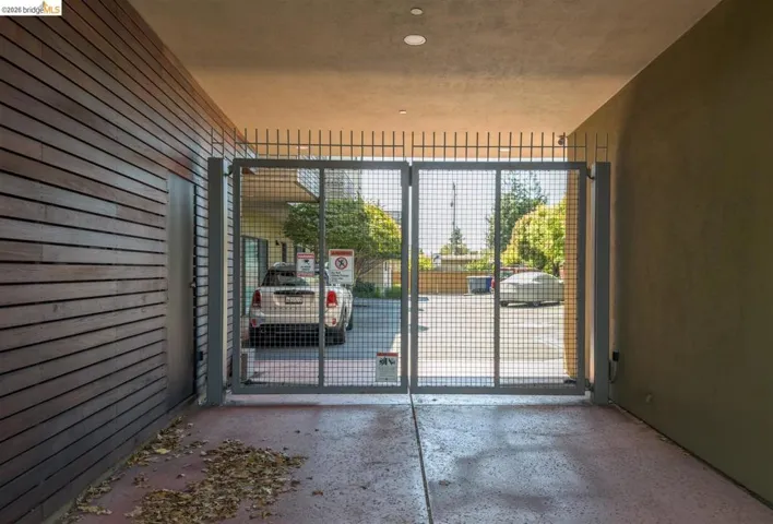 Gated entry to a covered parking area featuring a concrete floor, recessed lighting, a wood-slat accent wall, and a side access door