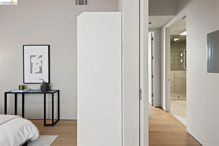 Warm wood-finish flooring extends through the hallway, featuring a modern bathroom with vertical tile accents, a glass shower enclosure, and recessed lighting