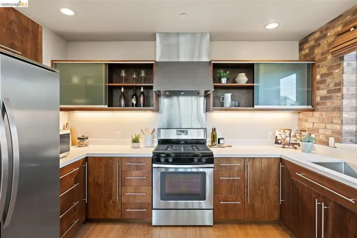 U-shaped kitchen featuring stainless steel appliances, wood-finish cabinetry, light countertops, and a brick accent wall