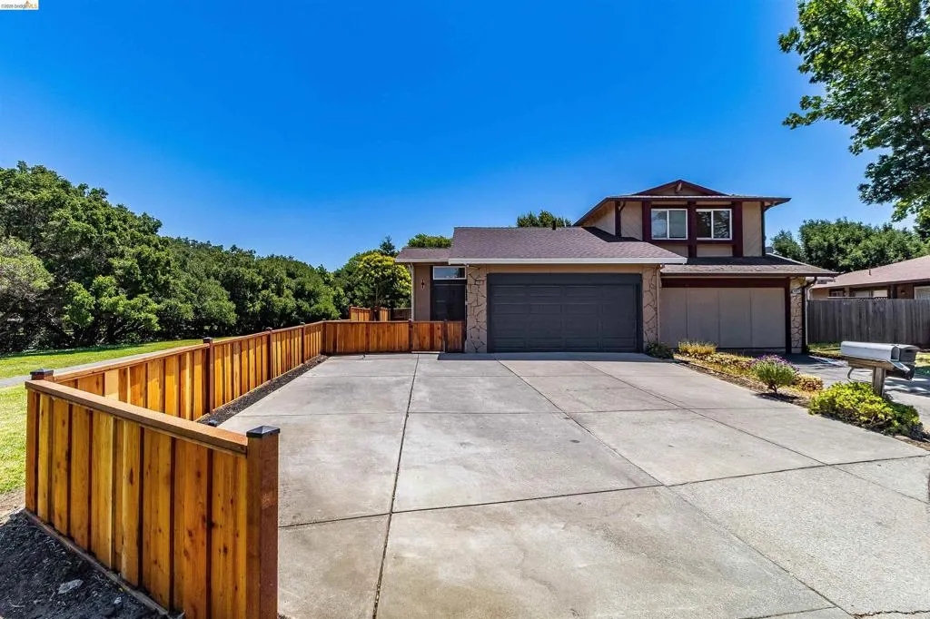 Multi-level residence featuring a two-car garage with a dark gray door, a stone-accented facade, and a concrete driveway