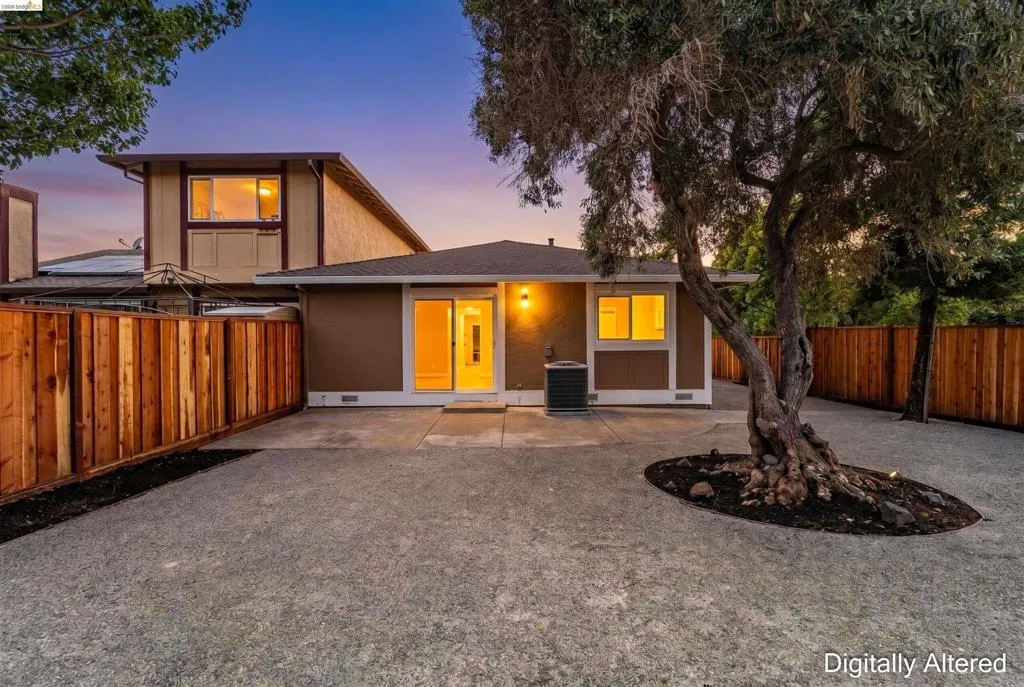 Paved patio area featuring a mature tree, new wood fencing, and a contemporary exterior with sliding glass doors and illuminated windows