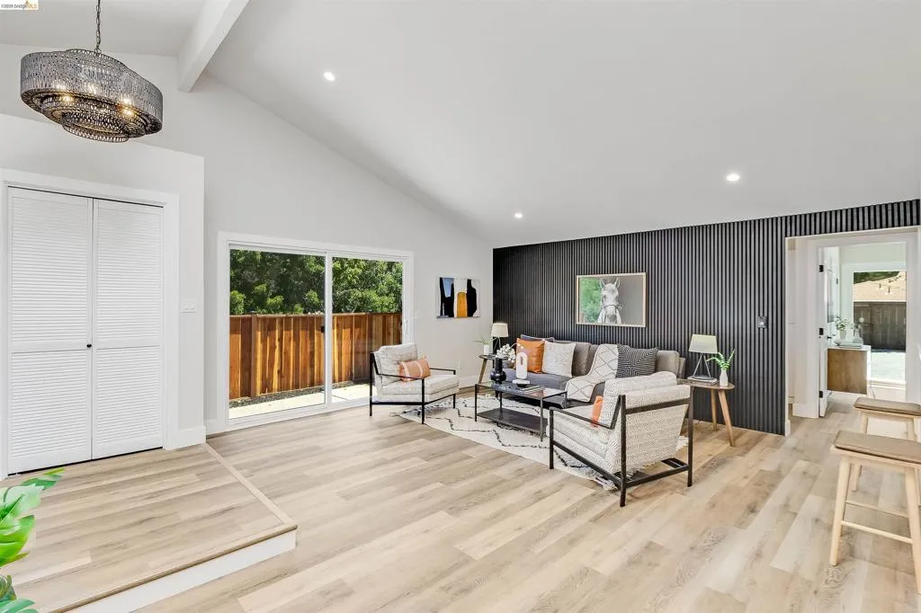 Spacious living area featuring light wood-finish flooring, vaulted ceilings, and a modern chandelier