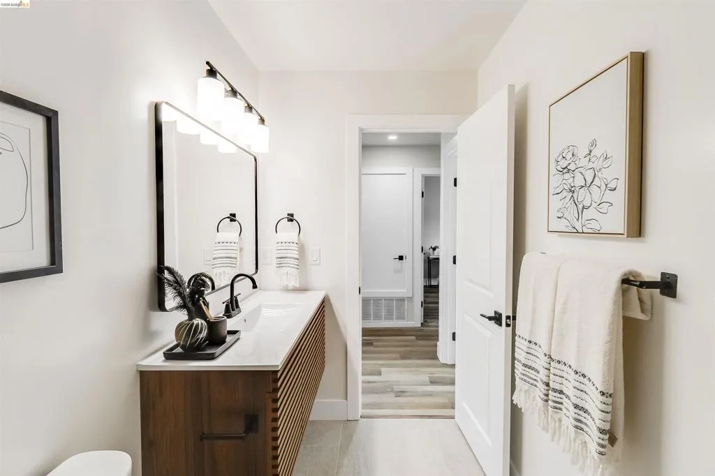 Bathroom featuring a wood-finish vanity with slat detailing and a white countertop, complete with a rectangular mirror and black wall-mounted faucet