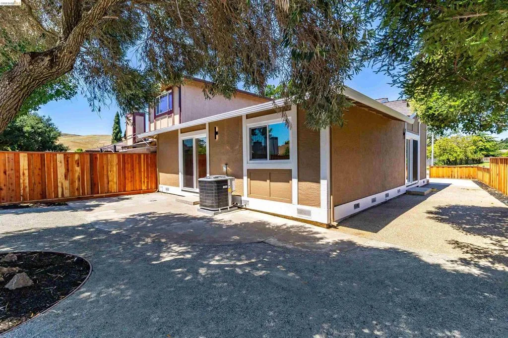 Rear exterior featuring a brown stucco finish with white trim, a wood privacy fence, and multiple sliding glass doors