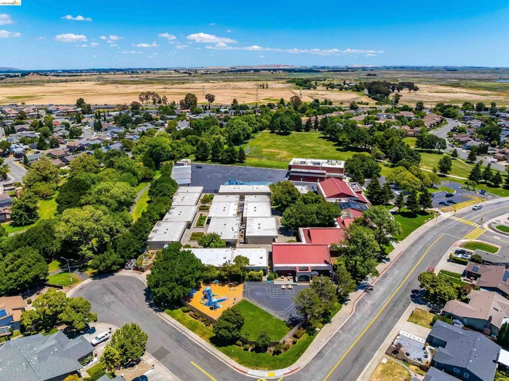 Expansive neighborhood featuring mature trees, residential properties, paved roads, and open fields in the background