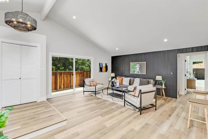 Spacious living area featuring light wood-finish flooring, vaulted ceilings, and a modern chandelier