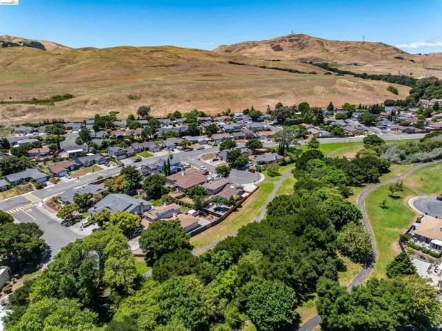 Residential neighborhood featuring single-story homes, mature trees, paved streets, and a backdrop of rolling hills