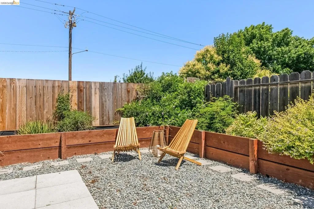 Enclosed backyard space featuring a gravel surface, square paver stones, and raised wood planter boxes