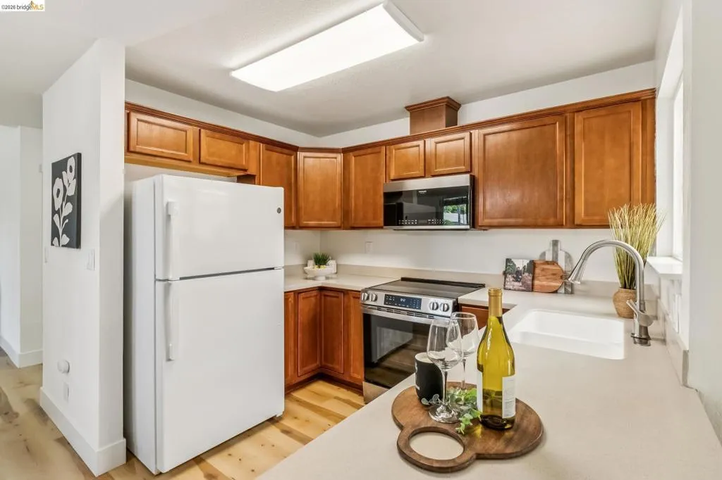Contemporary kitchen featuring wood cabinetry, light-toned countertops, a stainless steel microwave, and an undermount sink with a gooseneck faucet