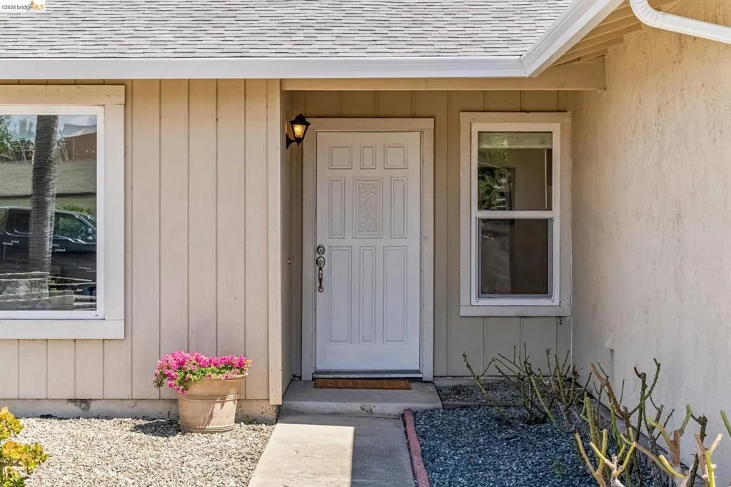 Entryway featuring a paneled door with decorative glass, an exterior wall sconce, and a concrete pathway