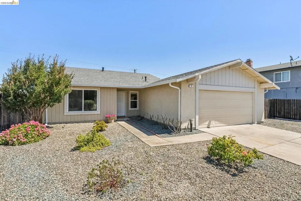 Single-story residence featuring a stucco exterior, attached garage, and a gravel front yard with mature shrubbery and plantings
