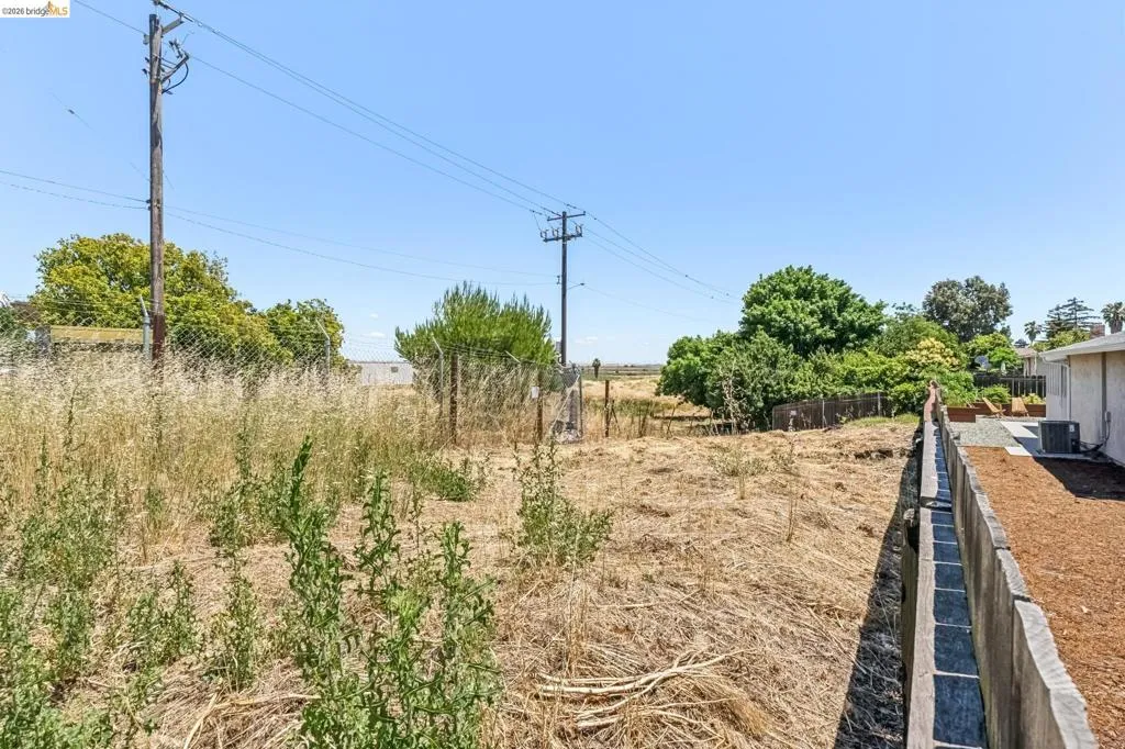 Expansive undeveloped lot featuring a chain link fence and a concrete retaining wall bordering an adjacent structure