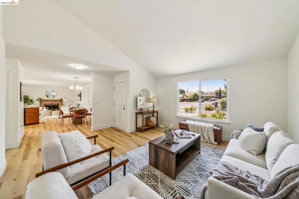 Spacious living area featuring light wood-finish flooring, a vaulted ceiling, and ample natural light from a large window