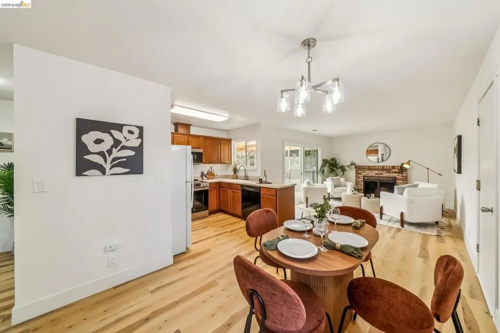 Open-concept living space featuring wood-finish flooring, a contemporary chandelier, a brick fireplace, sliding glass doors, and a kitchen with warm wood cabinetry