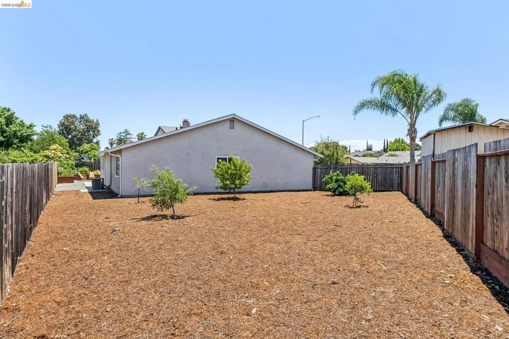 Spacious backyard featuring wood-chip landscaping, a wood privacy fence, and several small trees