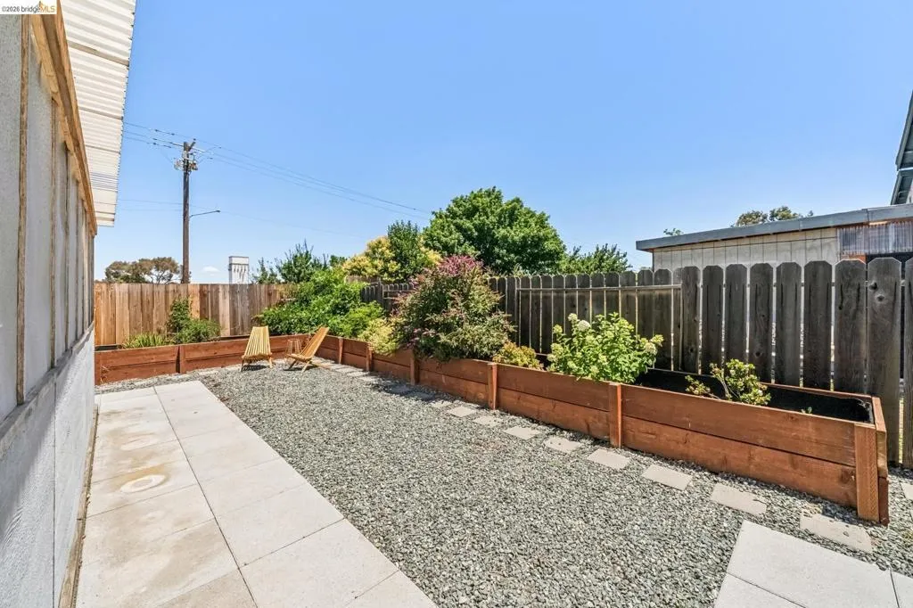 Private outdoor space featuring a gravel patio, concrete pathway, and multiple raised garden beds