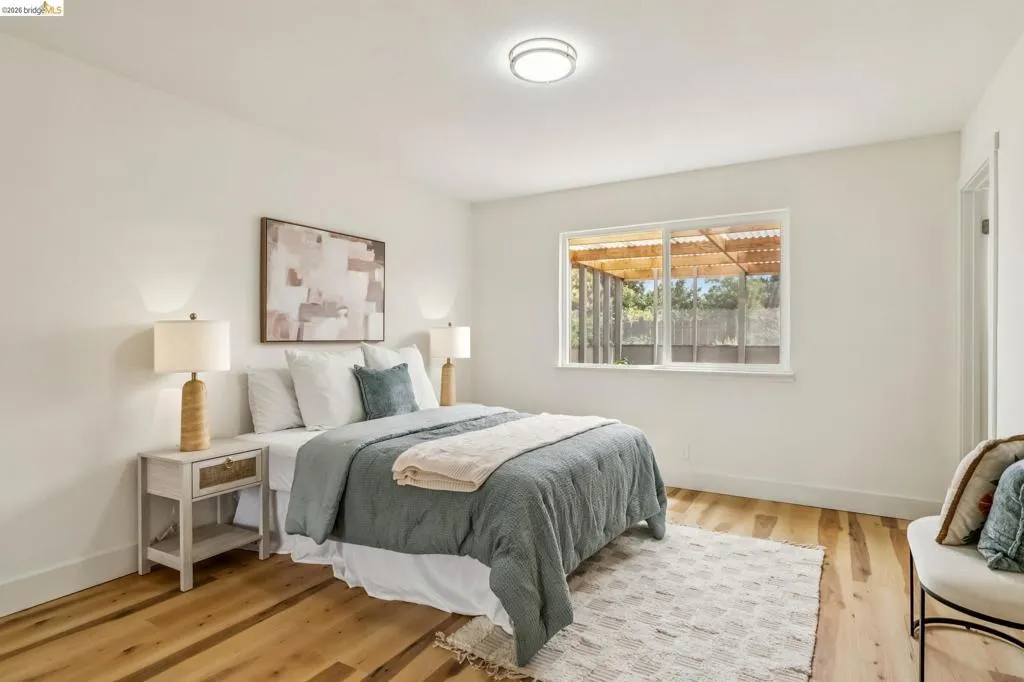 Bedroom featuring wood-finish flooring, a contemporary ceiling light fixture, a large window, and white trim