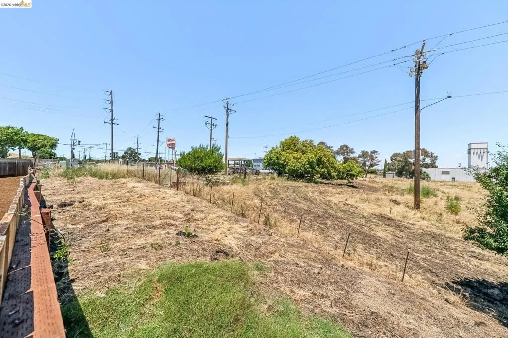 Expansive land parcel featuring varied terrain, a partial wooden fence, and scattered mature trees