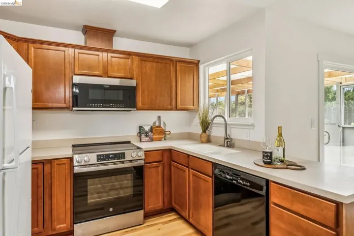 Kitchen featuring wood cabinetry, light countertops, stainless steel appliances, and wood-finish flooring