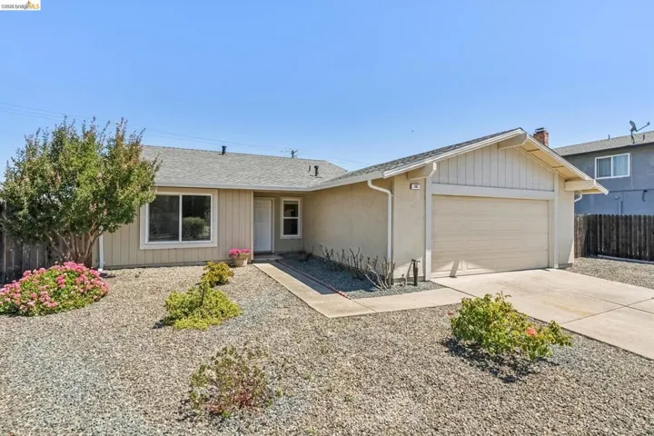 Single-story residence featuring a stucco exterior, attached garage, and a gravel front yard with mature shrubbery and plantings