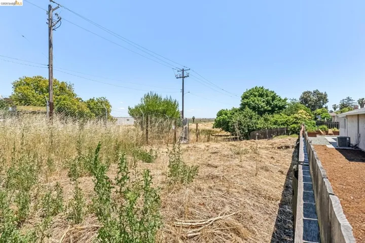 Expansive undeveloped lot featuring a chain link fence and a concrete retaining wall bordering an adjacent structure