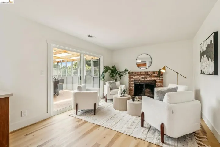 Spacious living area featuring light wood-finish flooring, a brick-surround fireplace, and white walls