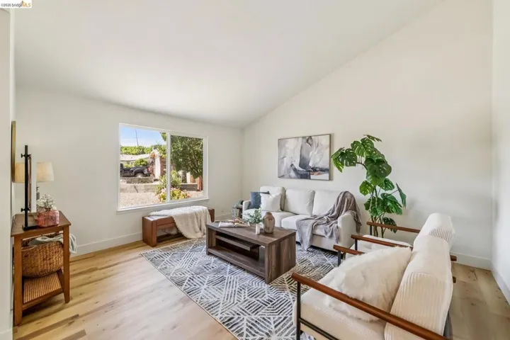 Bright living space featuring vaulted ceilings, light wood-finish flooring, a large window, and clean white walls