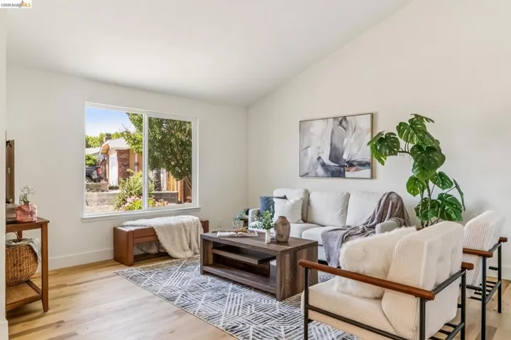 Living area featuring abundant natural light from a large window, light wood-finish flooring, a vaulted ceiling, and white wall finishes