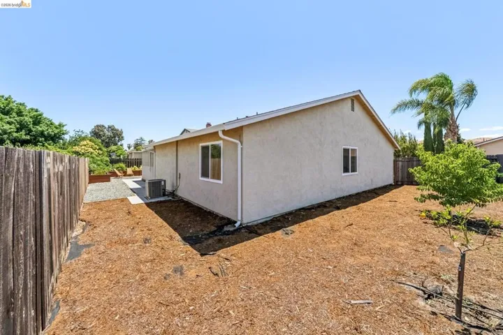Expansive backyard featuring a stucco exterior, white-framed windows, a concrete pad, a wooden fence, and a young tree