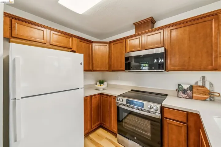 Kitchen featuring wood cabinetry, white countertops, stainless steel range, stainless steel microwave, and wood-finish flooring