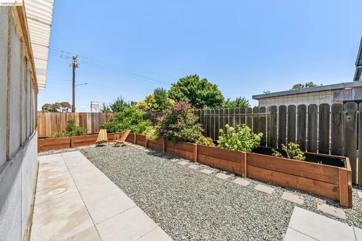 Private outdoor space featuring a gravel patio, concrete pathway, and multiple raised garden beds