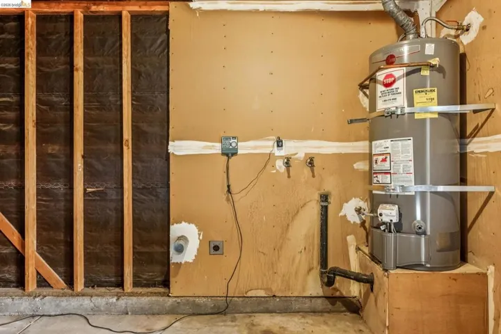 Utility area featuring a water heater, exposed wall framing, and concrete flooring