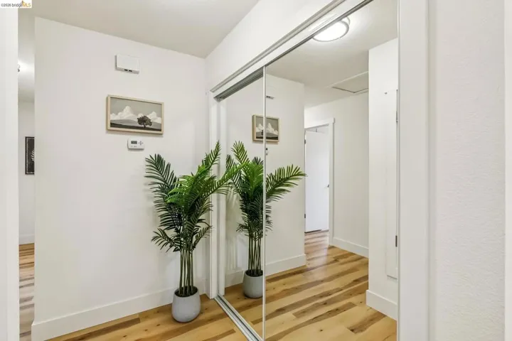 Reflective closet doors, wood-finish flooring, white baseboards, and neutral wall tones create a bright hallway