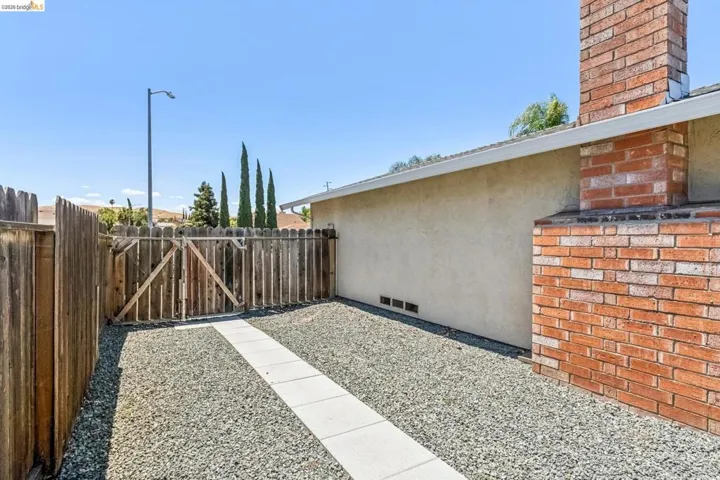 Side yard featuring a concrete paver walkway, gravel landscaping, and a wood privacy fence with gate access