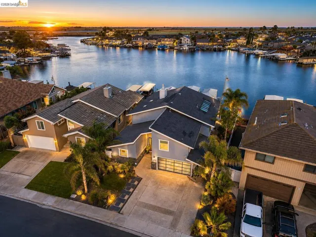 Waterfront property with private boat dock access, modern exterior featuring a two-car garage, manicured landscaping with integrated lighting, and a paved driveway