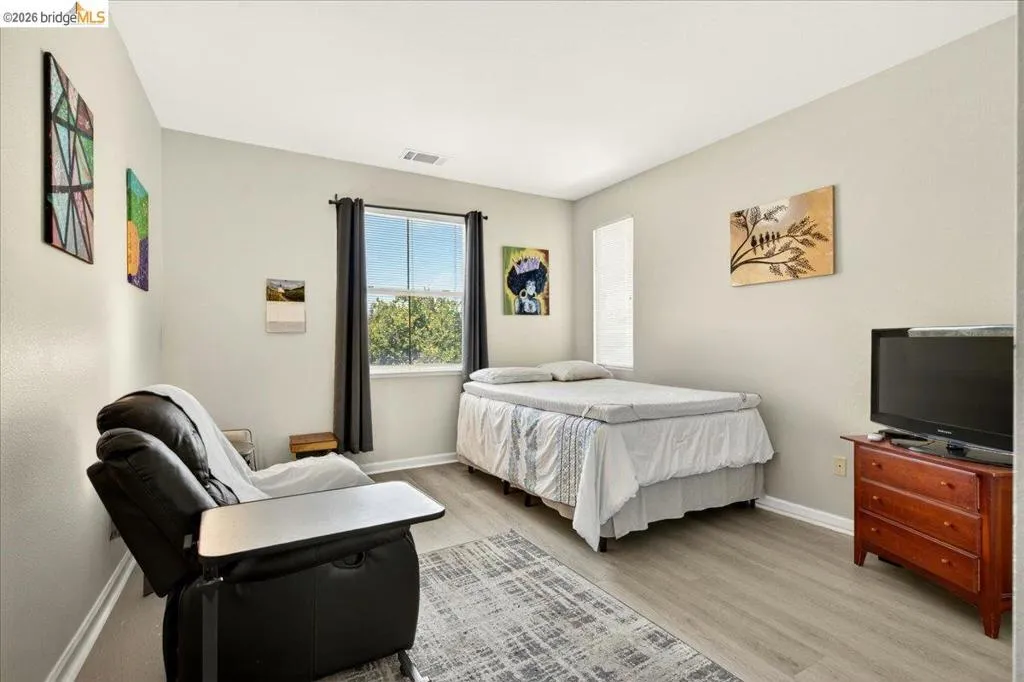 Bedroom featuring light gray wall paint, wood-finish flooring, a window with dark curtain rods, and white baseboards