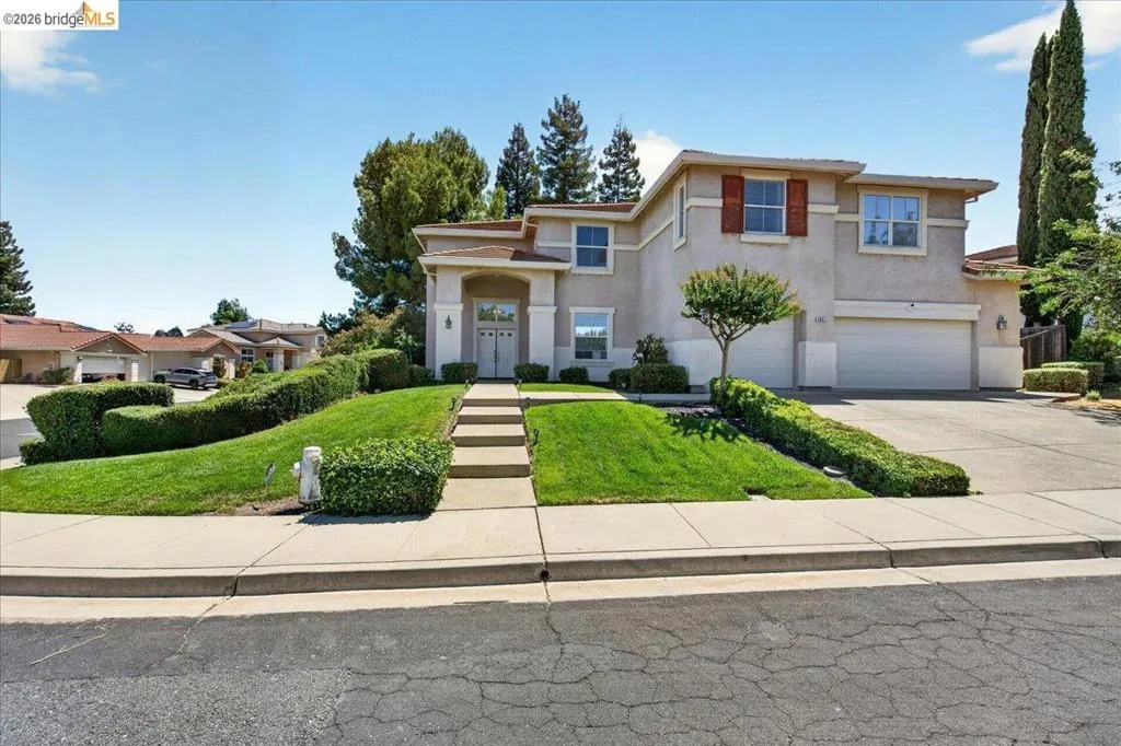 Two-story stucco residence with an arched entry, a concrete driveway, and a terraced front lawn
