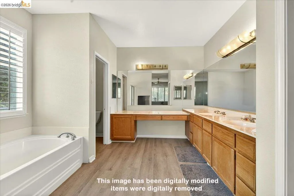 Spacious bathroom featuring a built-in soaking tub, wood-finish flooring, a double vanity with integrated sinks, and ample counter space with full-wall mirrors