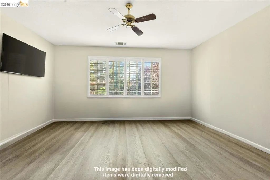 Spacious interior room featuring wood-finish flooring, neutral wall tones, and a ceiling fan