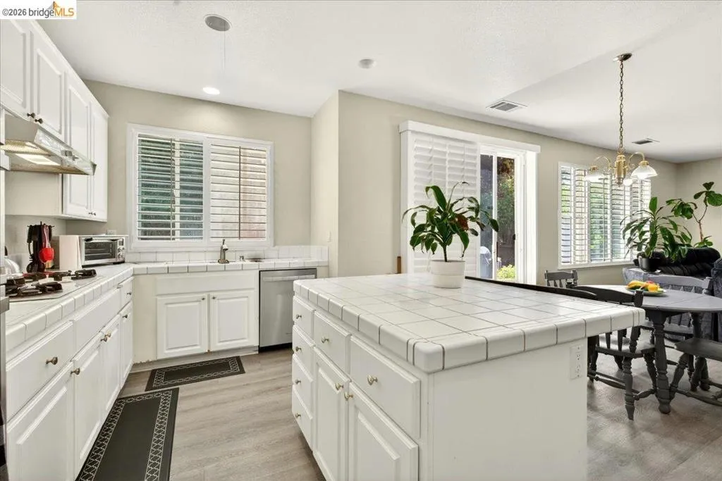 Kitchen featuring white shaker-style cabinetry, square tile countertops and backsplash, stainless steel appliances, and wood-finish flooring