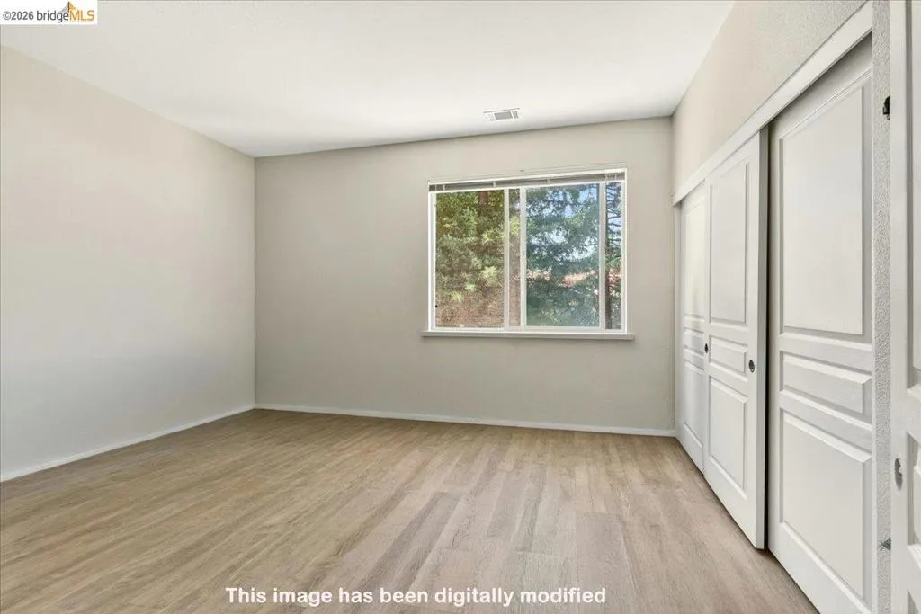 Spacious room featuring wood-finish flooring, light-colored walls, a large window, and sliding panel closet doors
