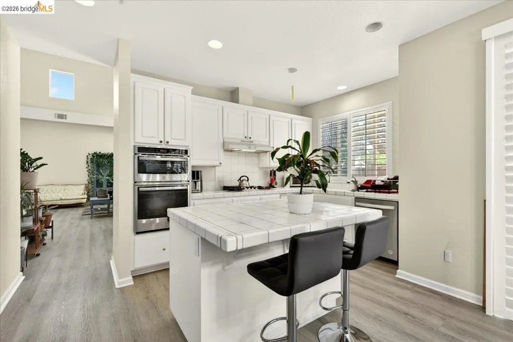 Kitchen featuring white cabinetry, tile countertops, stainless steel double ovens, and a built-in dishwasher