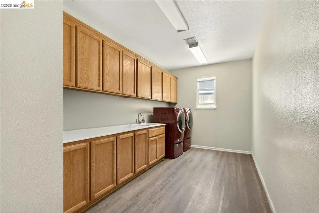Utility room featuring extensive wood cabinetry, a white countertop, a stainless steel sink with a chrome faucet, and wood-finish flooring