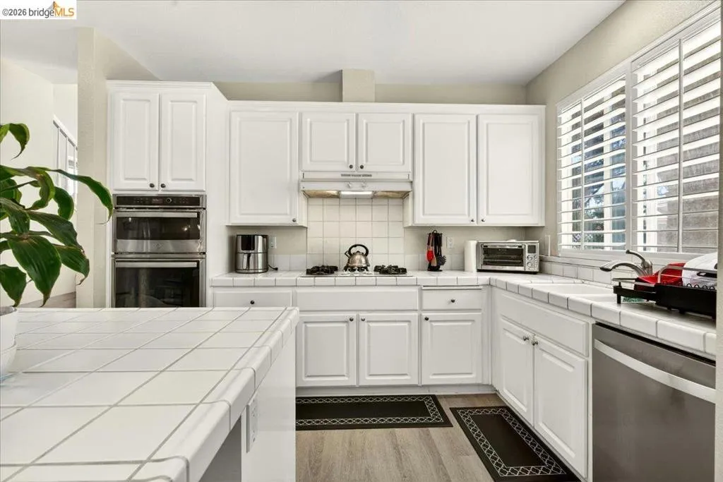 Kitchen featuring white cabinetry, built-in double ovens, a tile backsplash, tile countertops, and wood-finish flooring