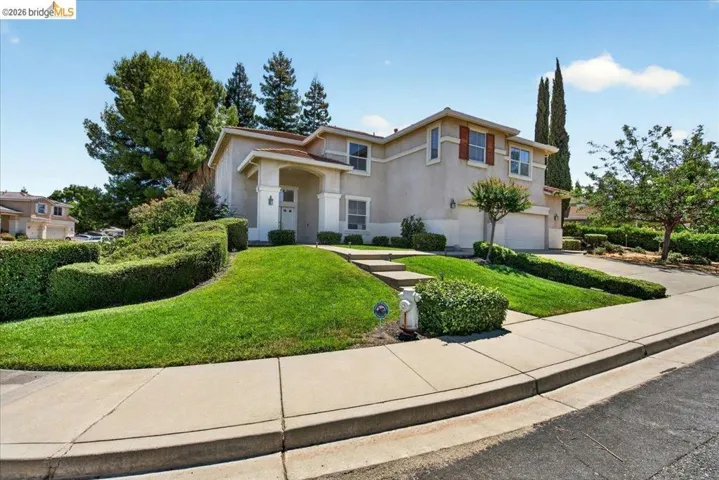 Two-story stucco residence with a two-car garage, mature landscaping, and a concrete driveway
