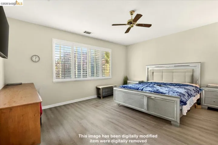 Spacious room featuring wood-finish flooring, a contemporary ceiling fan, and large windows with plantation shutters