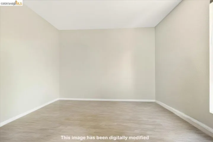 Spacious interior room with light-colored walls, wood-finish flooring, and white baseboards