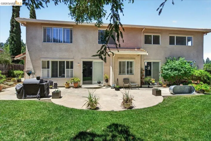 Spacious backyard featuring a large concrete patio, expansive lawn area, and mature landscaping