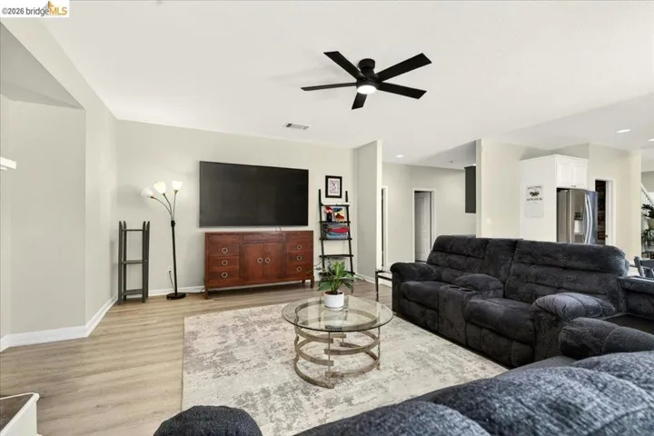 Spacious living area featuring light wood-finish flooring, neutral wall tones, and a modern black ceiling fan
