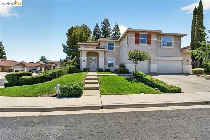 Two-story stucco residence with an arched entry, a concrete driveway, and a terraced front lawn